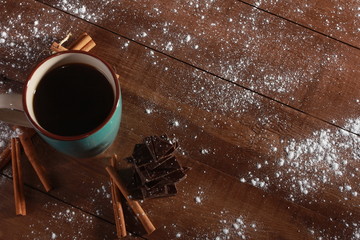 Coffee, cinnamon sticks, pieces of chocolate and sugar powder on vintage wooden table. Coffee break concept. Blue cup, winter drink, espresso, top view