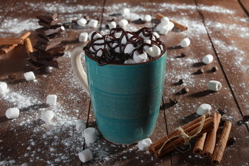 Cocoa, marshmallow, cinnamon sticks, pieces of chocolate and sugar powder on vintage wooden table. Desserts, sweets or coffee shop concept. Blue cup, winter drink, side view, confection