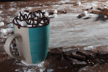 Cocoa, marshmallow, cinnamon sticks, pieces of chocolate and sugar powder on vintage wooden table. Desserts, sweets or coffee shop concept. Blue cup, winter drink, side view, confection