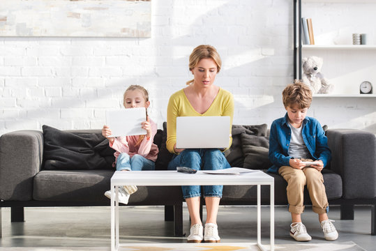 mother and beautiful children sitting on sofa and using digital devices