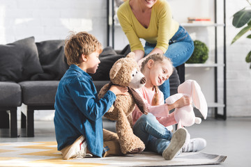 cropped shot of happy mother sitting on couch and cute little children playing with toys at home