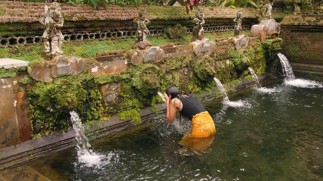 Young Woman Praying at Holy Spring Water Temple. Traditional Balinese Hindu Spiritual Ceremony of Purification. 4K Slowmotion. Gugung Kawi, Bali, Indonesia.