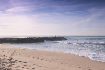 Sandy beach at the sunset with a stone jetty with a fisherman in background