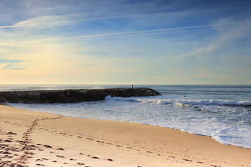 Sandy beach at the sunset with a stone jetty with a fisherman in background