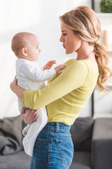 side view of beautiful mother holding adorable infant child at home