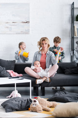 mother with infant child meditating in lotus position and looking at camera while naughty kids...