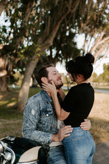 Loving Adorable Portrait of two Attractive Good Looking Young Adult Modern Fashionable People Guy Girl Couple on Classic Green Motorcycle Hugging, Kissing, Holding, and Looking into each Other’s Eyes 