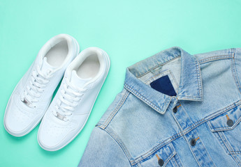 Retro style denim stylish jacket and white hipster sneakers on a mint-colored paper background. Minimalism, top view,flat lay