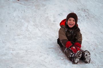 Sincere children's emotions. Сhild ride down a snow hill in winter. Winter fun sliding down...