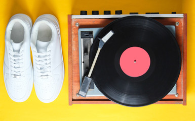 Pop culture. White hipster sneakers, vinyl player on a yellow background. Retro style. 80s. Top...