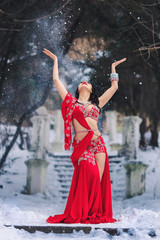 Fototapeta premium beautiful young girl dancing belly dance in red dress in winter in a park on the snow.