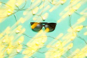 Stylish sunglasses with a light effect offset from the garlands on a blue background. Top view,...