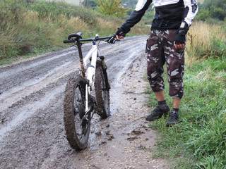 adult man with a dirty mountain bike on a country road. back view.