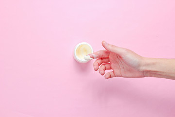 Female hand takes a moisturizing and softening cream for face skin on a pink background. Minimalism..