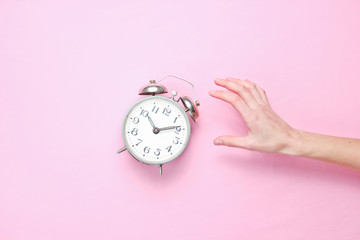 Female hand takes alarm clock on pink background. Top view. Time to wake up. Minimalism.