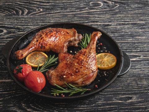 Juicy roasted duck legs with with tomato and lemon in a fry pan , black surface, close up