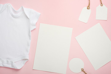 Fototapeta premium Layout Flat Lay white baby bodysuit shirt, on a pink background, for a girl with white postcards and tags.Mock up for design and placement of logos, advertisements