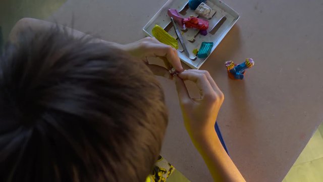 Boy is sitting at the desk and sculpting figures with colored plasticine. Development of children fine motor skills