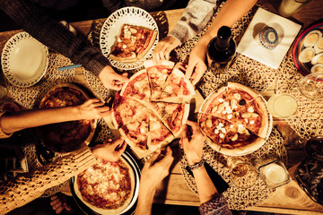 Top view of friends taking a slice of pizza and eat dinner together in friendship - people at home - table top view from above - sharing food with men and women