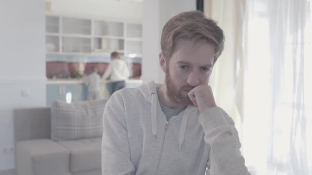 Portrait of sad bearded man standing in living room close up. Woman and boy are in the background. Family relationships. Family problems. Slow motion.