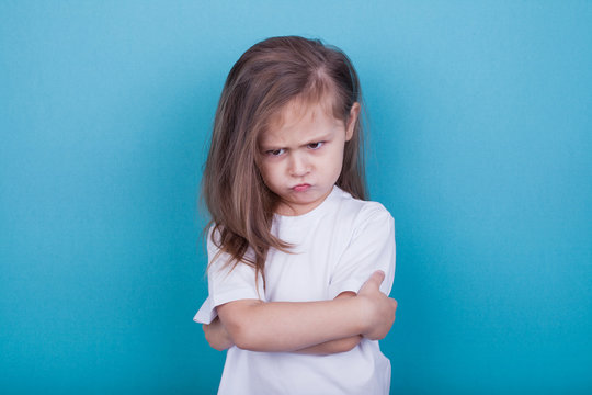 The little girl on a blue background was offended by folding her arms and frowning eyebrows