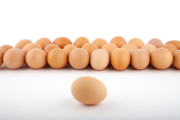 A group of brown chicken eggs with one egg ahead on white background, perspective view