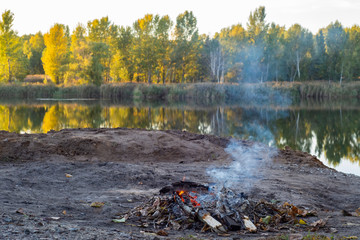 A small fire is burning on the shore of a beautiful lake.