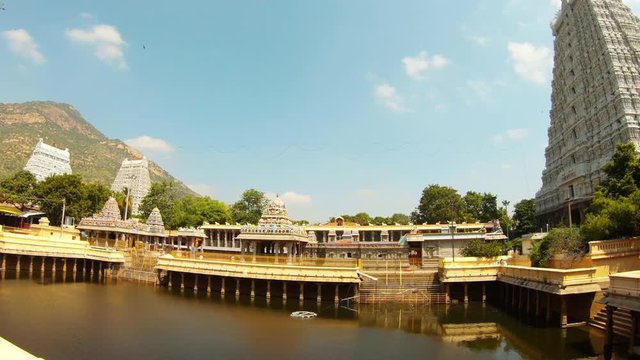 Pond among sculptural towers of southern temple complex Tiruvannamalai holy mountain Arunachala on background reflection in water