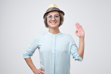 Friendly-looking european teenager dressed in blue shirt saying hello, waving her hand. Positive human emotions, feelings or facial expressions