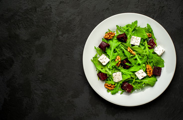 Salad of arugula, cheese, beet, walnut, on the background of slate, stone or concrete.