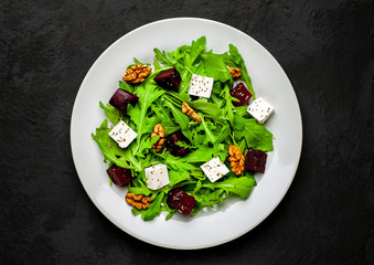 Salad of arugula, cheese, beet, walnut, on the background of slate, stone or concrete.