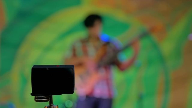 Little action video camera recording ethnic open air concert. Bass guitar player on blurry abstract bokeh background