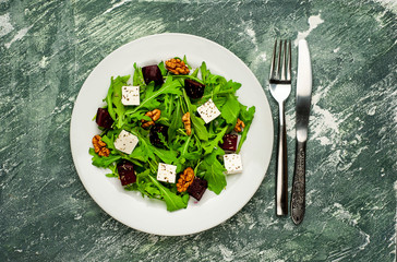 Salad of arugula, cheese, beet, walnut, on the background of slate, stone or concrete.