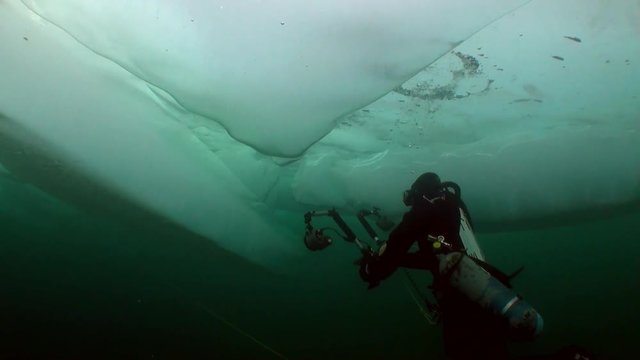 Diver cameraman under ice in cold water as concept of extreme underwater sports and active lifestyle of lake Baikal.