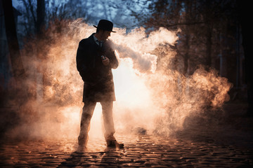 Vaping man in black hat holding a mod. A cloud of vapor.