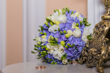 wedding rings lie and beautiful bouquet as bridal accessories.Two golden rings and wedding flowers. Greeting card, invitation,colorful flowers white and blue freesia and hydrangea. Copy space