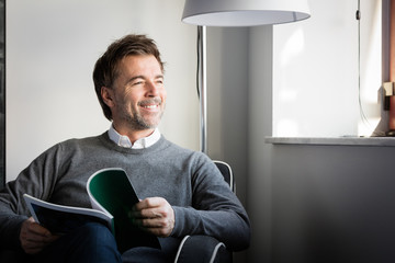 Handsome smiling man reading in a sofa looking at the window  
