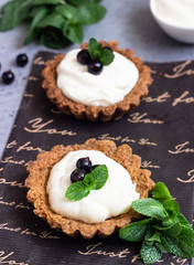 Mini tarts (tartlets) with whipped cream or custard and fresh berries served with mint. Homemade dessert. Grey background. Copy space.