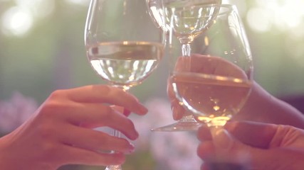 Group of people toasting and drinking white wine on the restaurant terrace. Glasses with wine over sunset background. Slow motion 4K UHD video 3840x2160