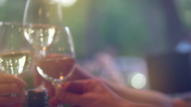 Group of people toasting and drinking white wine on the restaurant terrace. Glasses with wine over sunset background. Slow motion 4K UHD video 3840x2160