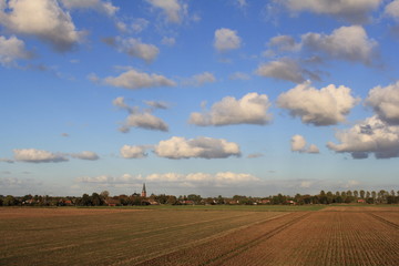 Fototapeta premium a little village in the dutch countryside with ploughed land in front and a blue sky with white clouds in the background