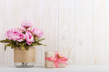 Pink flowers in a vase and a gift in craft paper on the table. Concept of Women's Day or St. Valentine.