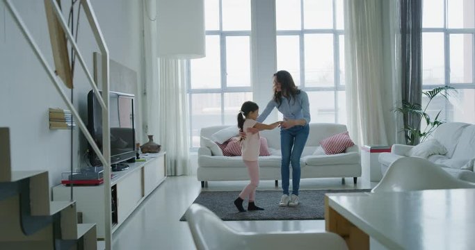 Portrait of happy mother and daughter having fun dancing together in living room in slow motion. Shot with RED camera in 8K. Concept of happy family, childhood, parenthood