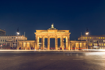Obraz premium Brandenburg Gate of Berlin at night with rear view. Lanterns illuminate the street. Light from passing cars is visible. the monument is illuminated by light.