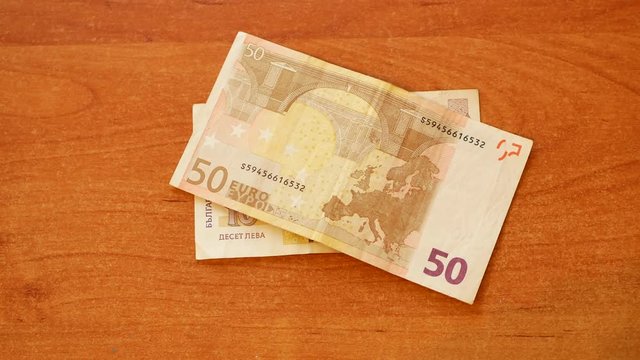 man put Bulgarian lev banknote on wooden desk and put 50 Euros on top and clap his hand on pile as a symbol of Bulgaria and European Union integration. close-up 4k video footage POV