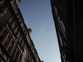 Two parallel buildings with sky between, bisected by vapour trail on a sunny evening