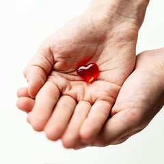 One small red plastic heart in a hand on daylight. Symbol of love and care.