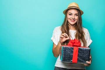 Happy young woman in dress holding gift box and looking at the camera while enjoys over blue background