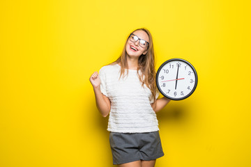 Young pretty woman in striped jacket holding clock isolated on yellow background