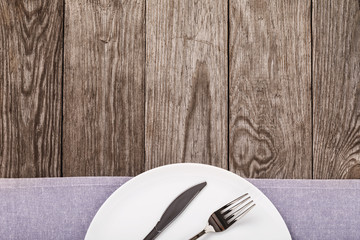 Cutlery and empty white ceramic plate on wooden table with copy space, top view